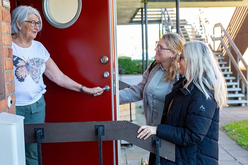Kvinna i 77-årsåldern öppnar dörren för två kvinnor från kommunen.