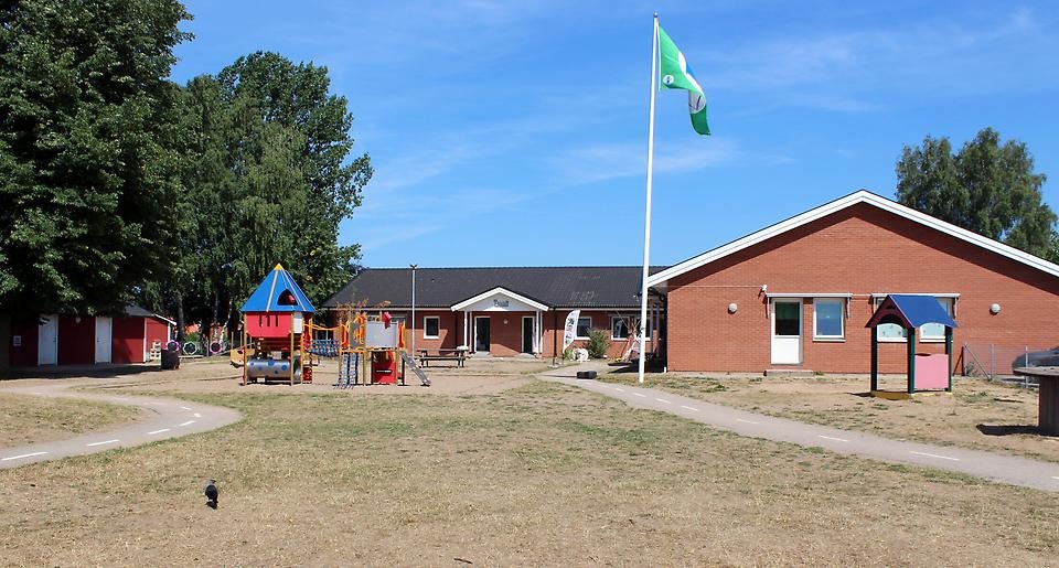 Förskolan Linneas skolgård. Förskolebyggnaden syns i bakgrunden och på gården är en stor gräsmatta och en sandlåda med klätterställning.