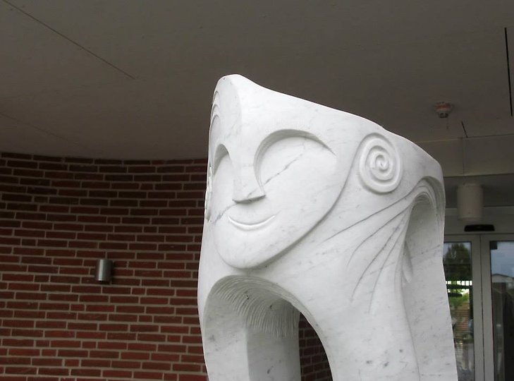 Skulptur vit marmor abstrakt ansikte framför röd tegelvägg