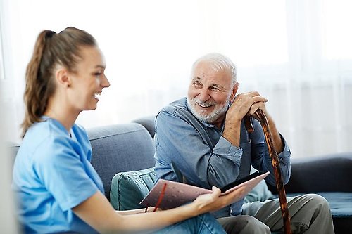 En vårdare samt äldre man sitter på en soffa.