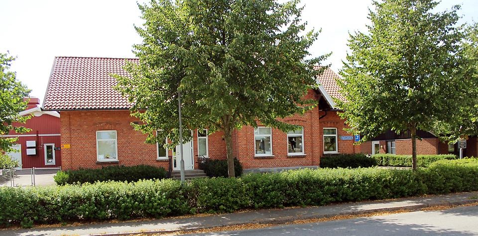 Bakom ett par lummiga träd är en brun tegelbyggnad som är Pilagårdens förskola.
