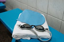 Simglasögon, handduk och en blå badmössa på en blå bänk framför en vitkaklad vägg.