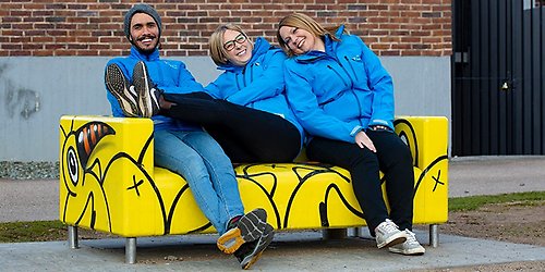 Mobila teamet, två kvinnor en man med blåa jackor, sitter på en gul Klippan-soffa.