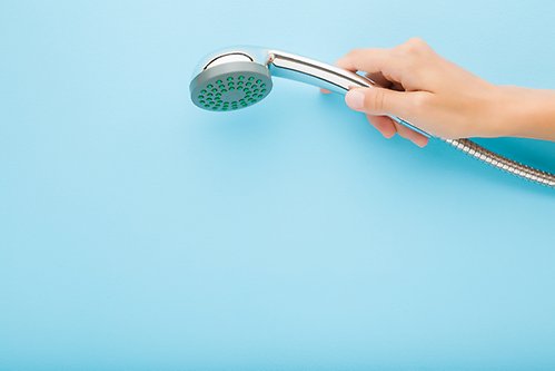 En bild på en hand som håller ett duschmunstycke mot ljusblå bakgrund.