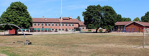 Vedby skolas skolgård. En stor gräsmatta med fotbollsmål syns framför skolbyggnaden.