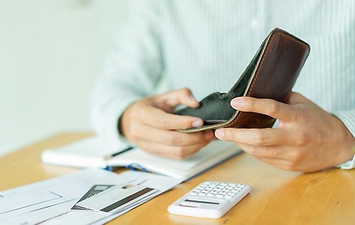 En man som sitter vid ett bord och ser över sin ekonomi genom att titta in i en tom plånbok.