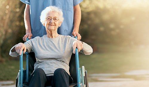 Äldre dam blir puttad i rullstol av en vårdare.